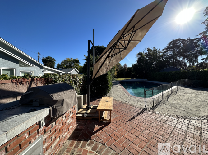 A patio with a table and an umbrella is in front of a pool.