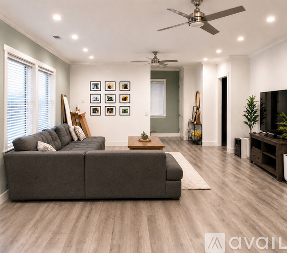 A living room with a grey sofa, a fan, and a painting on the wall.