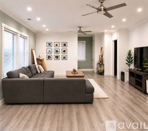 A living room with a grey sofa, a fan, and a painting on the wall.