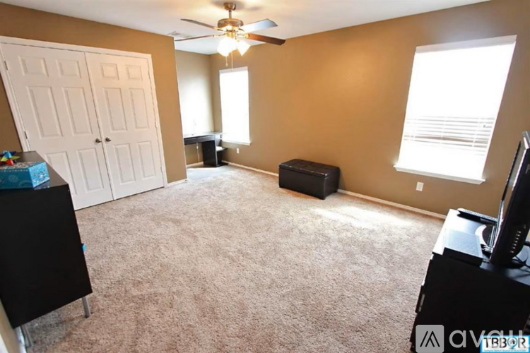 A living room with a white door, a brown wall, a ceiling fan, and a black ottoman.