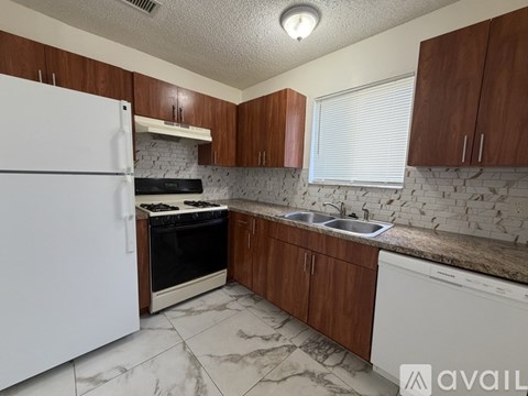 A kitchen with a white fridge, brown cabinets, and a marble countertop.