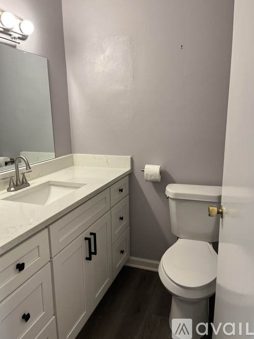A white toilet with a gold flush handle is in a bathroom with a sink and mirror.