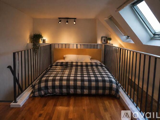 A bed with a checkered comforter is in a room with a skylight.