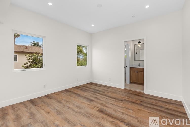 A spacious room with wooden flooring and white walls, with a view of a house through a window.