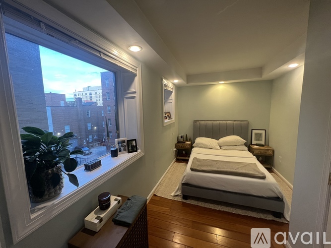A bedroom with a bed, nightstand, and window overlooking a cityscape.