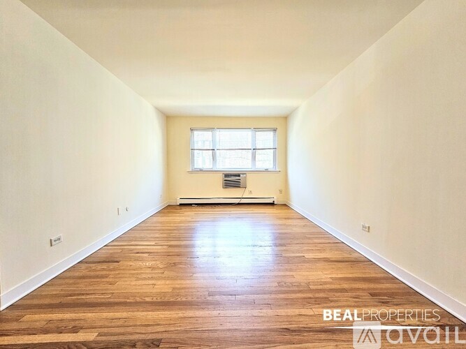 A spacious room with wooden flooring and a window.