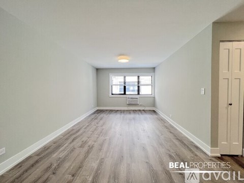 A spacious room with wooden flooring and a window with blinds.
