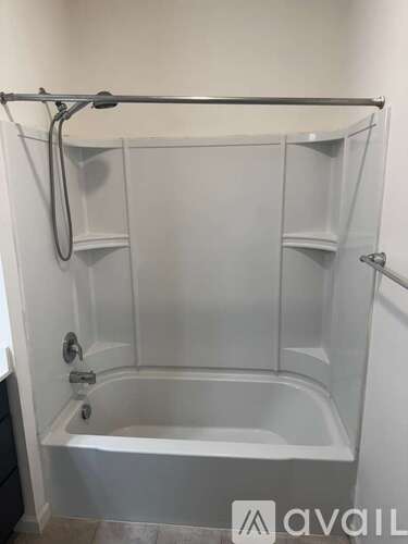 A white bathtub with a glass shower door and a glass shelf above it.