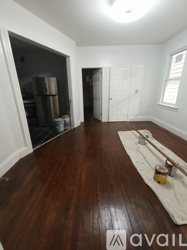 A room with wooden floors and white walls, with a doorway leading to another room.