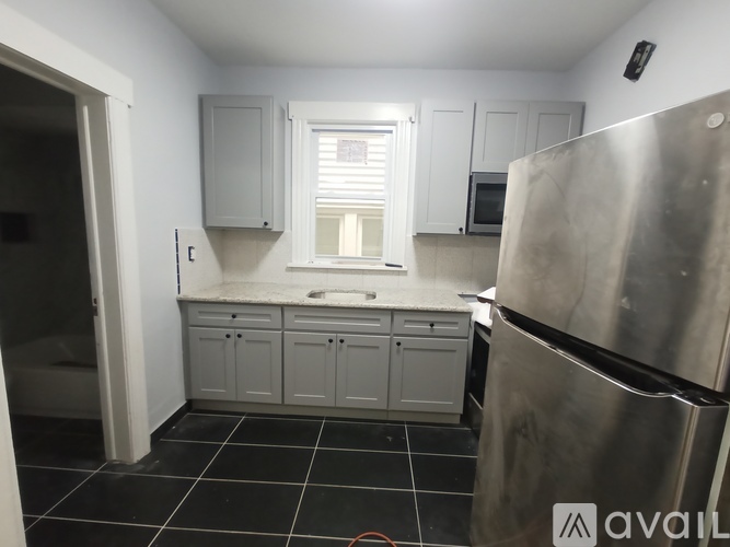 A kitchen with a refrigerator, cabinets, and a window.