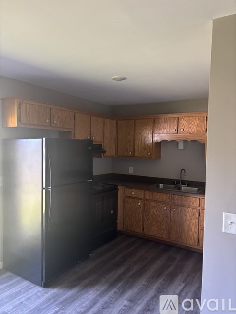 A kitchen with a black refrigerator and wooden cabinets.