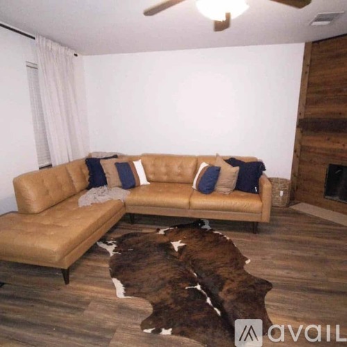 A tan leather couch with blue pillows sits in a room with a cowhide rug.