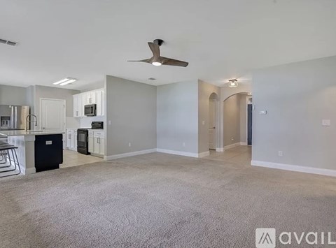 A spacious living room with a kitchen in the background and a carpet on the floor.
