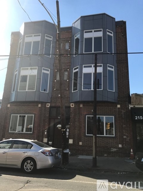 A grey car is parked in front of a two-story building.