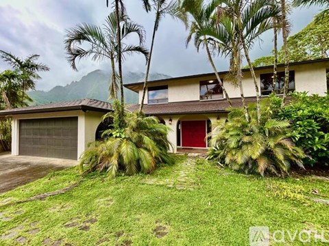 A house with a red door is surrounded by greenery and palm trees.