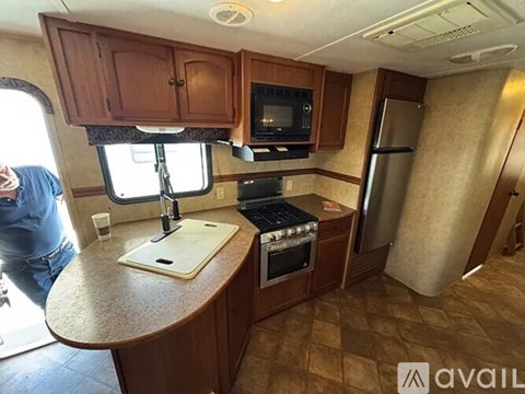 A man is standing in a kitchen with wooden cabinets and a stove top oven.