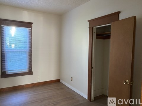 A room with a wooden floor, a window with blinds, and a door.