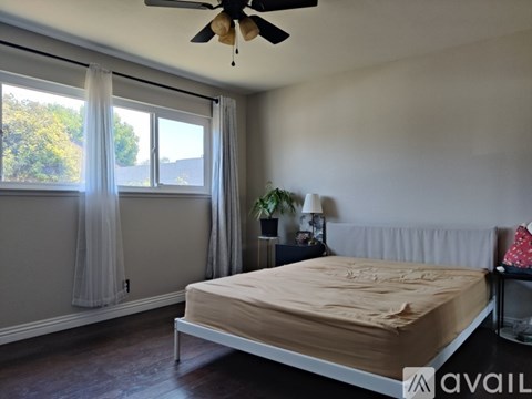 A bedroom with a bed, a ceiling fan, and a window with curtains.