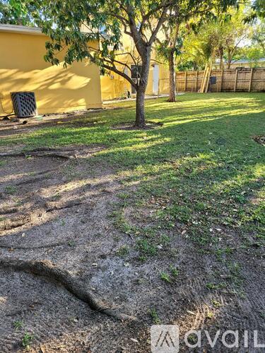 A tree in a yard with a yellow house in the background.