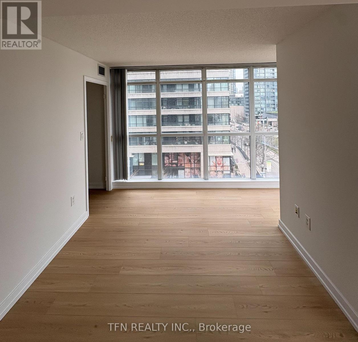 A room with wooden flooring and a large window overlooking a cityscape.