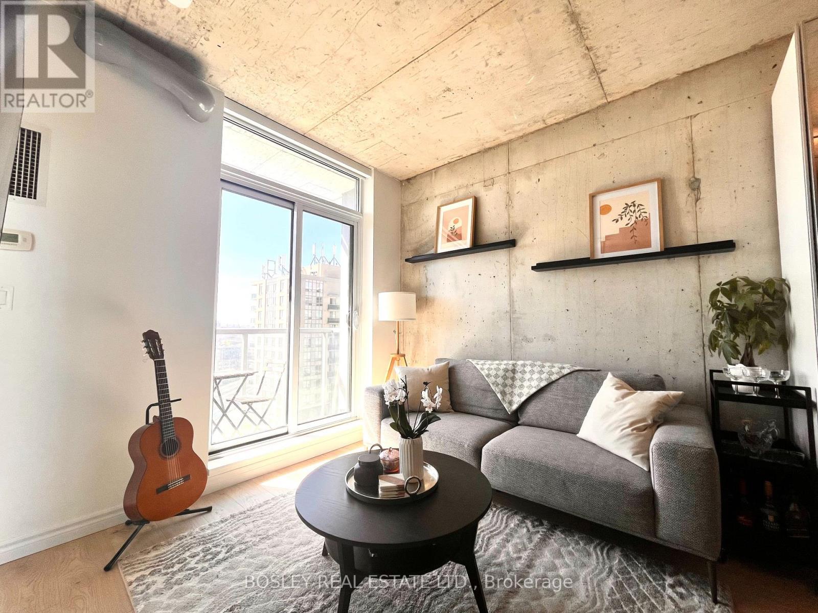 A living room with a grey couch, a guitar, a table with a vase and a lamp.