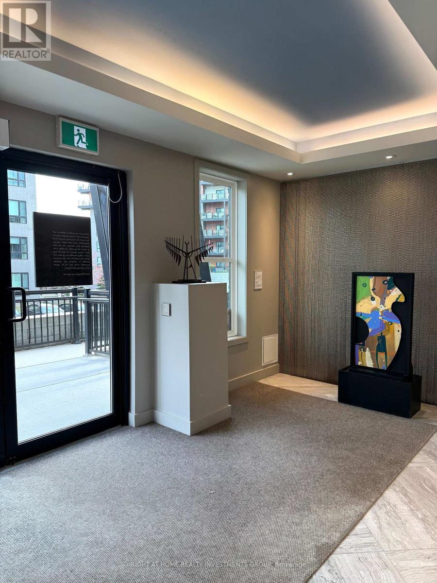 A hallway with a carpeted floor, a door with a window, a plant, and a painting on the wall.