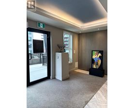 A hallway with a carpeted floor, a door with a window, a plant, and a painting on the wall.
