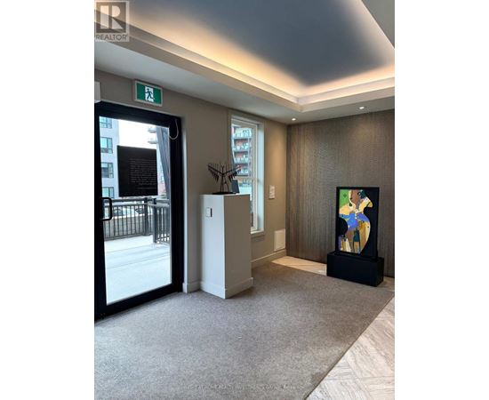 A hallway with a carpeted floor, a door with a window, a plant, and a painting on the wall.