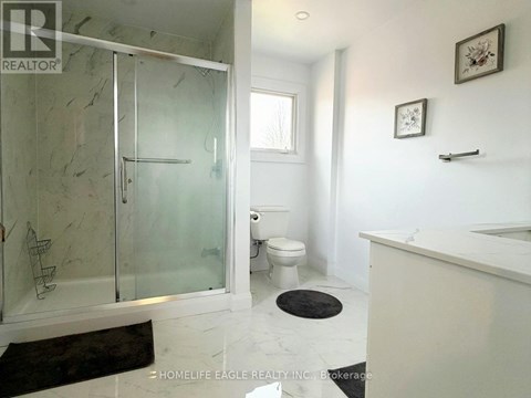 A bathroom with a glass shower stall and a toilet.