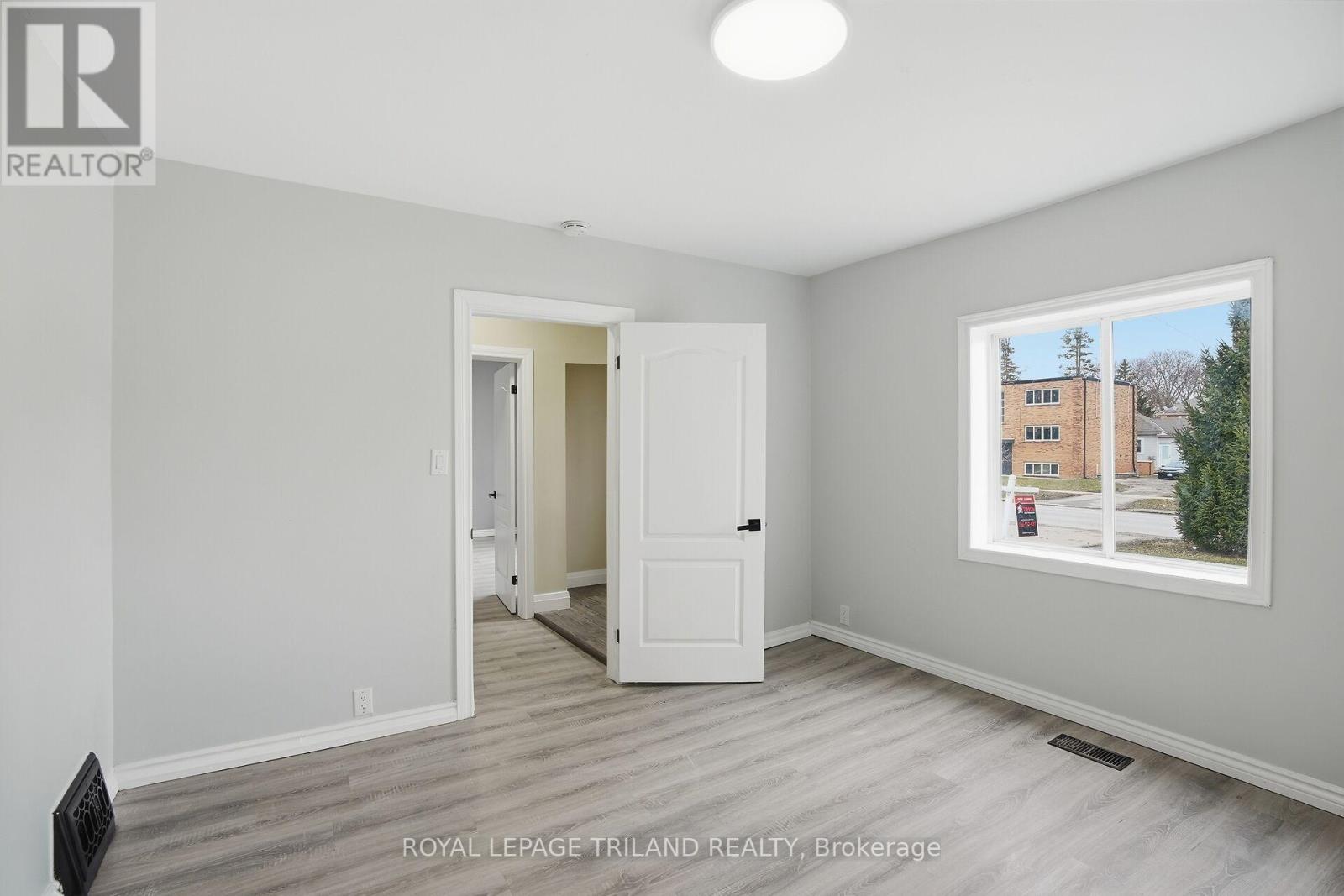 A room with a doorway leading to another room, a window with a view of a building and trees outside, and a logo for Royal LePage Triland Realty, Brokerage.