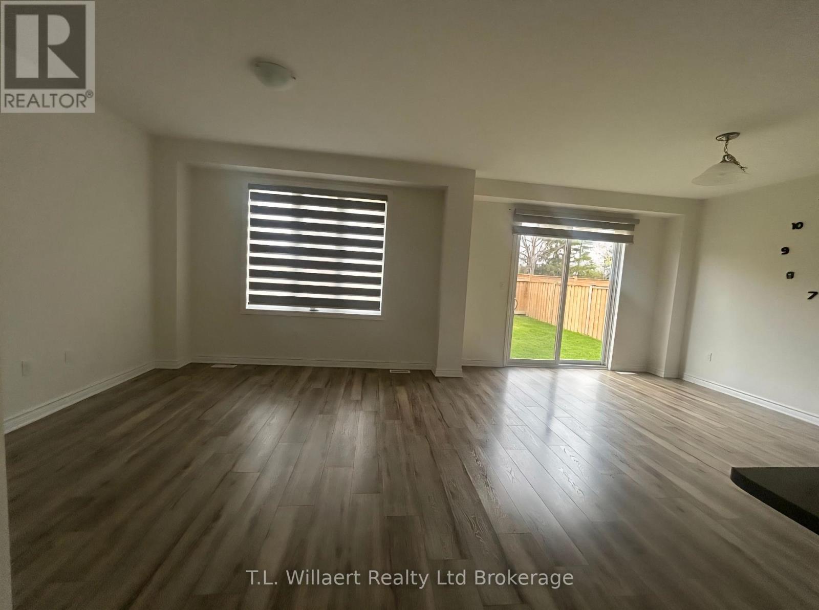 A room with wooden flooring and a sliding glass door leading to a backyard.