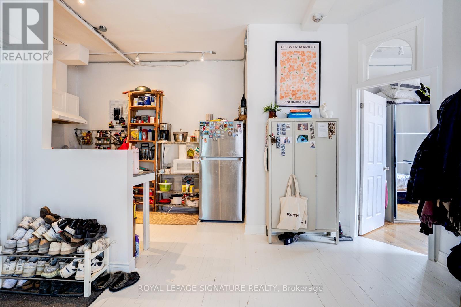 A kitchen with a refrigerator and a pile of shoes.