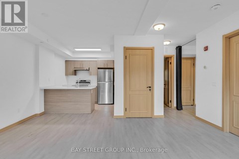A spacious room with wooden floors and white walls, featuring a kitchenette with a sink and refrigerator.