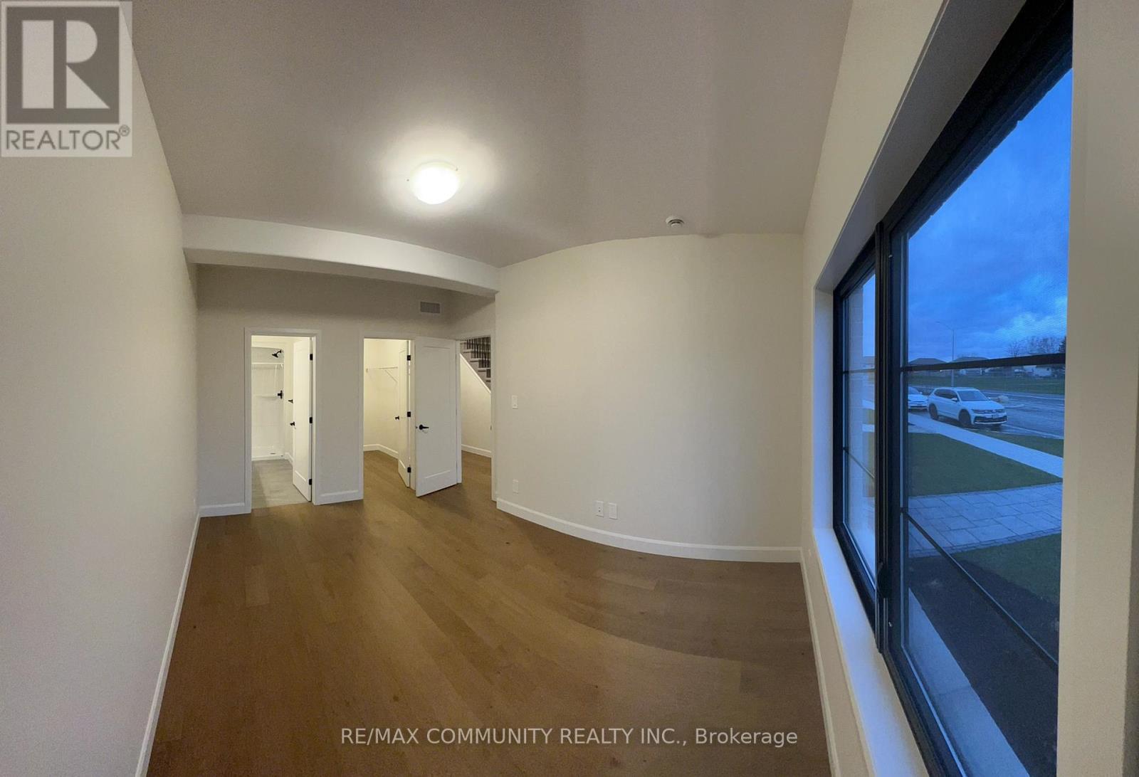 A spacious room with wooden flooring and white walls, with a view of the outside through a large window.