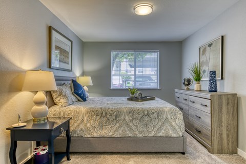 A bedroom with a bed, nightstand, and a window.