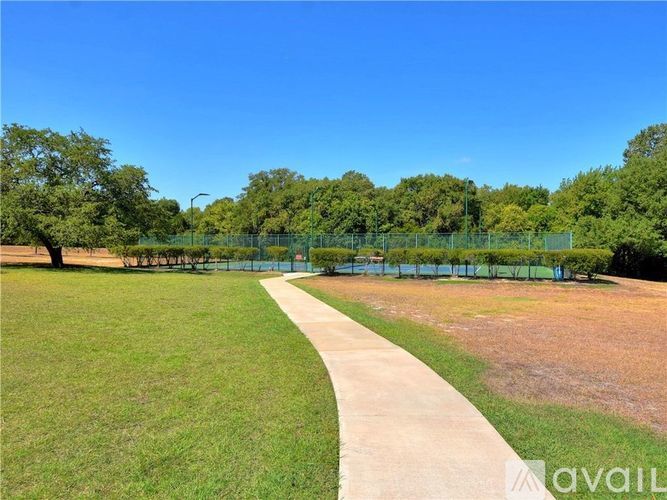A park with a walking path, green grass, and trees.