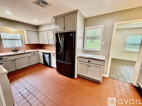 A kitchen with brown tiles and a black fridge.