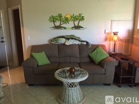 A living room with a grey couch and a wall mural of palm trees.