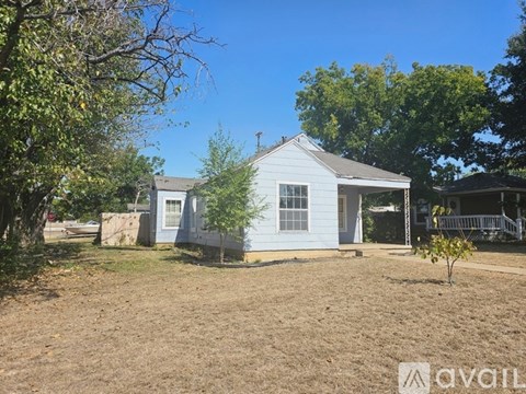 A blue house with a white fence and a tree in front.