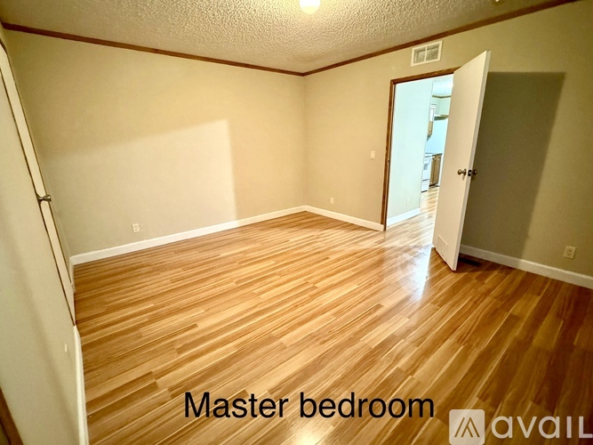 A master bedroom with wooden flooring and a doorway leading to another room.