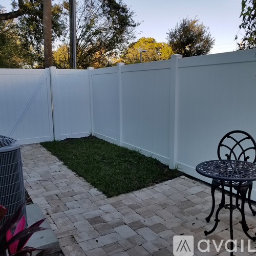 A patio with a white fence, a table and chairs, and a brick walkway.