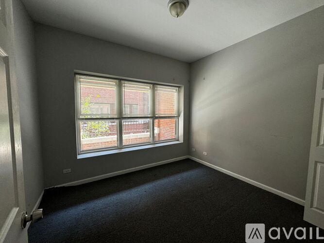 A room with a carpeted floor and a window with a view of a building outside.