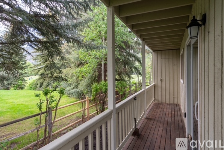 A wooden porch with a view of a green lawn and trees.
