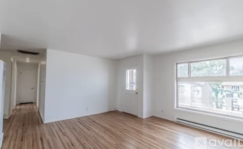 A room with wooden floors and white walls, with a window showing a view of other buildings.