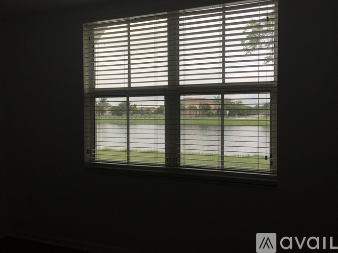 A window with blinds overlooking a grassy field.