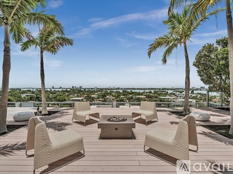 A patio with chairs and a table is surrounded by palm trees.