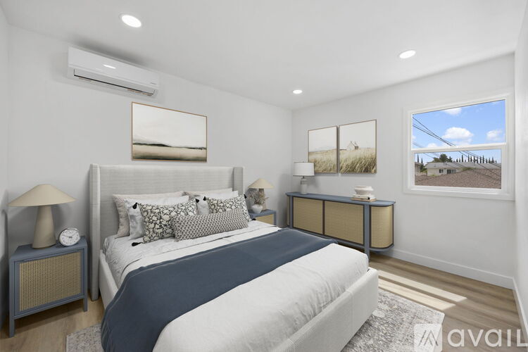 A bedroom with a large bed, nightstands, and a window showing a view of a house and trees.