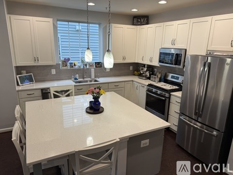 A kitchen with white cabinets and a white island with a vase of flowers on it.