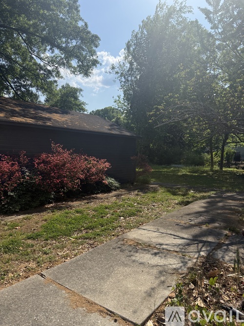 A concrete pathway leads to a building with a roof and a tree with red leaves.