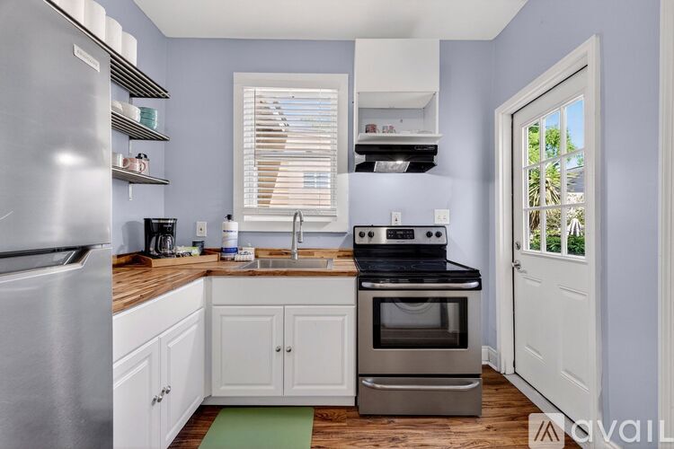 A kitchen with a stainless steel refrigerator, a sink, a stove, and white cabinets.